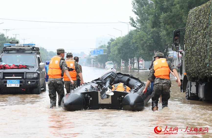 8月2日上午，在涿州市107國道受災路段，數(shù)十名武警某部官兵到達現(xiàn)場準備為受困群眾送去食品、飲用水。圖為武警官兵正在搬運沖鋒舟。 宋燁文攝