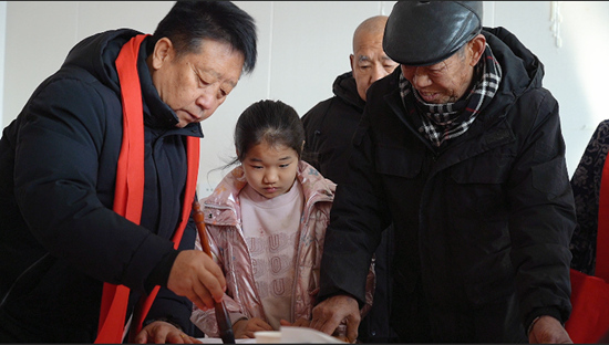 曲陽縣下河鎮(zhèn)新赤岸村民們圍繞在書法家旁邊觀看寫對聯(lián)、領(lǐng)取春聯(lián)。張?zhí)飰褦z